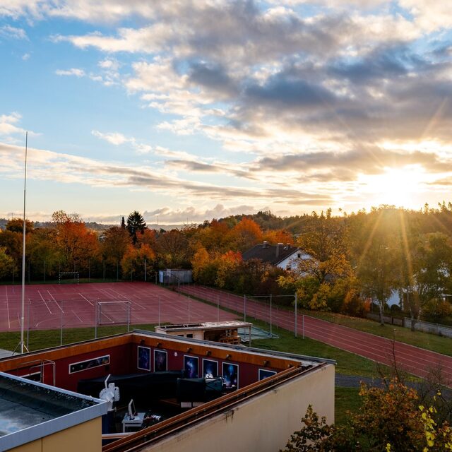 Sonnenaufgang über der geöffneten Beobachtungsbühne der Sternwarte Hof und den umliegenden Sportanlagen